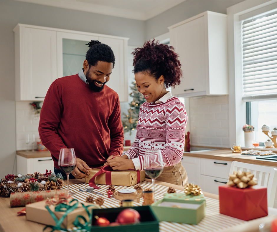 Man and woman wrapping holiday gifts in their kitchen
